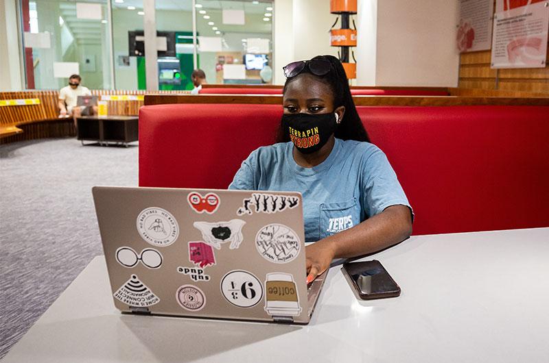 student wearing a terrapin strong mask working on her laptop sitting in a booth
