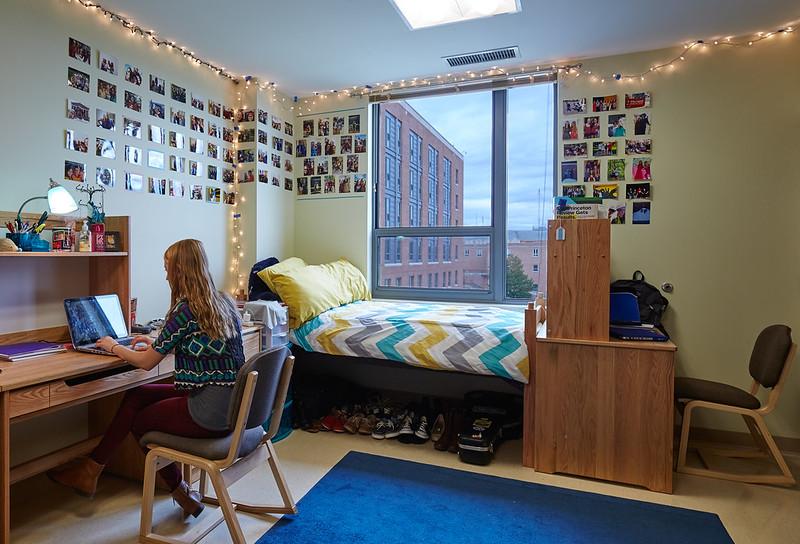 student working at her desk in a decorated residence hall room with a large window