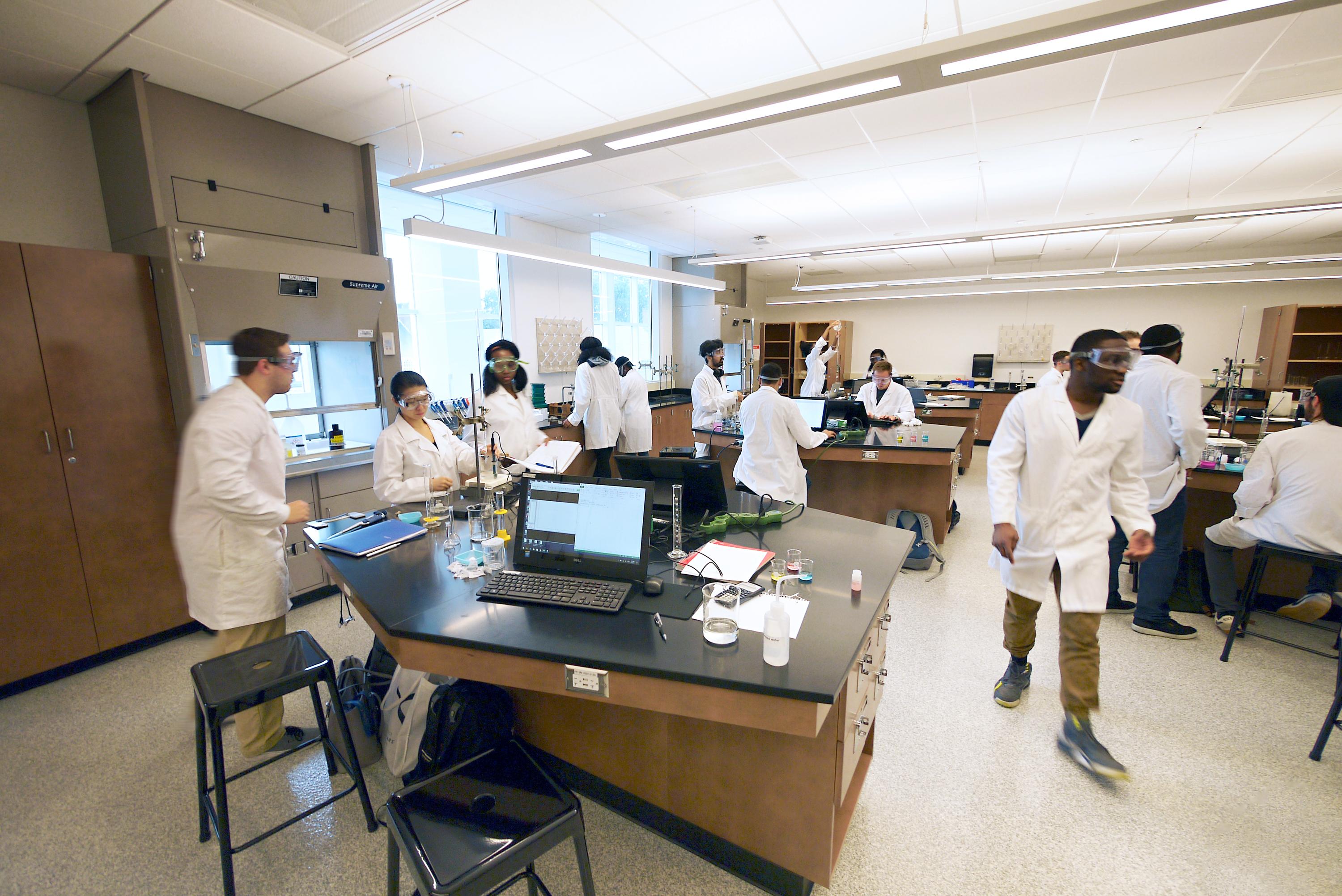 students working in a chemistry lab wearing goggles and white lab coats