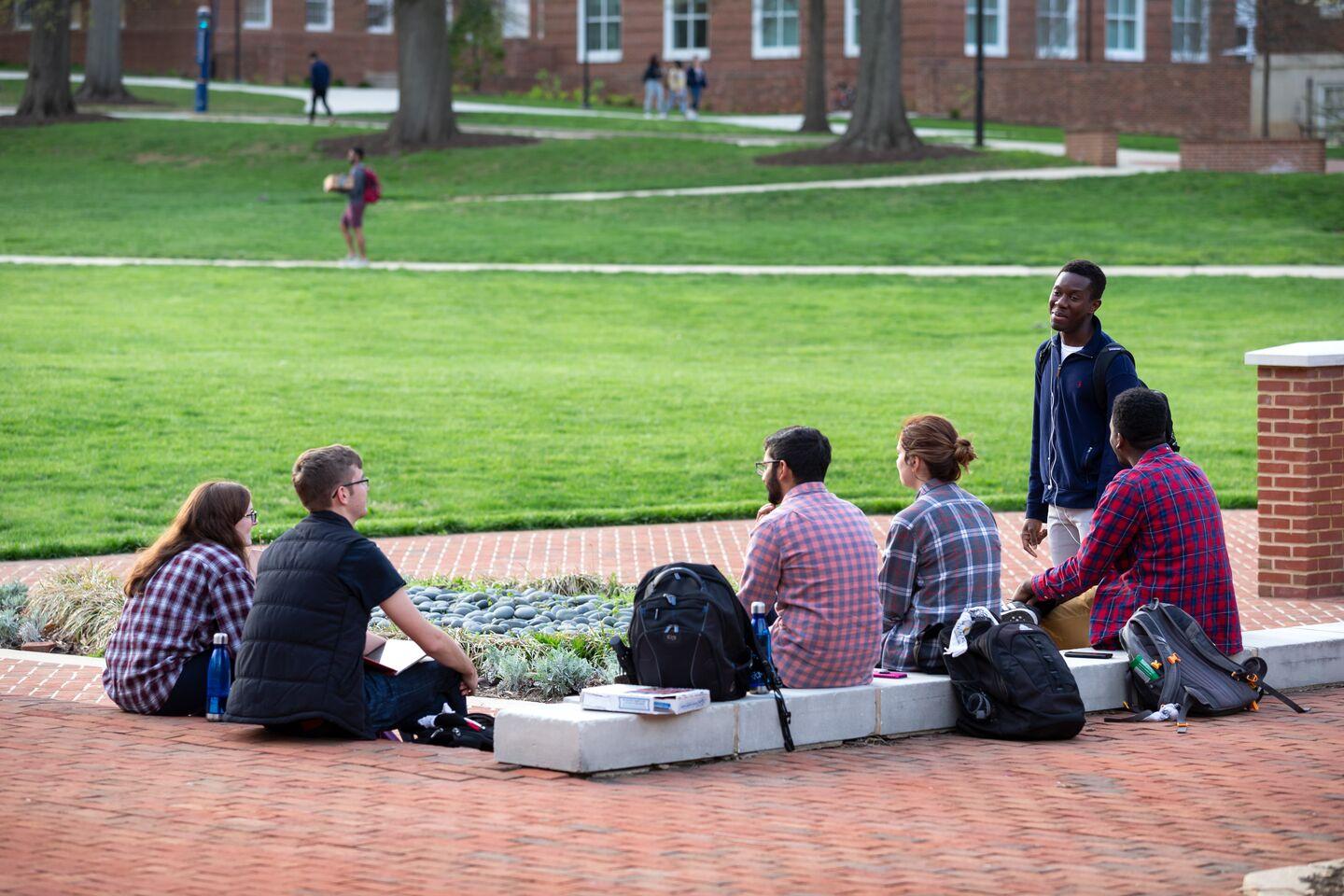 A group of students sitting outdoors on the Mall in the evening hours at dusk in front of Main Administration Building.