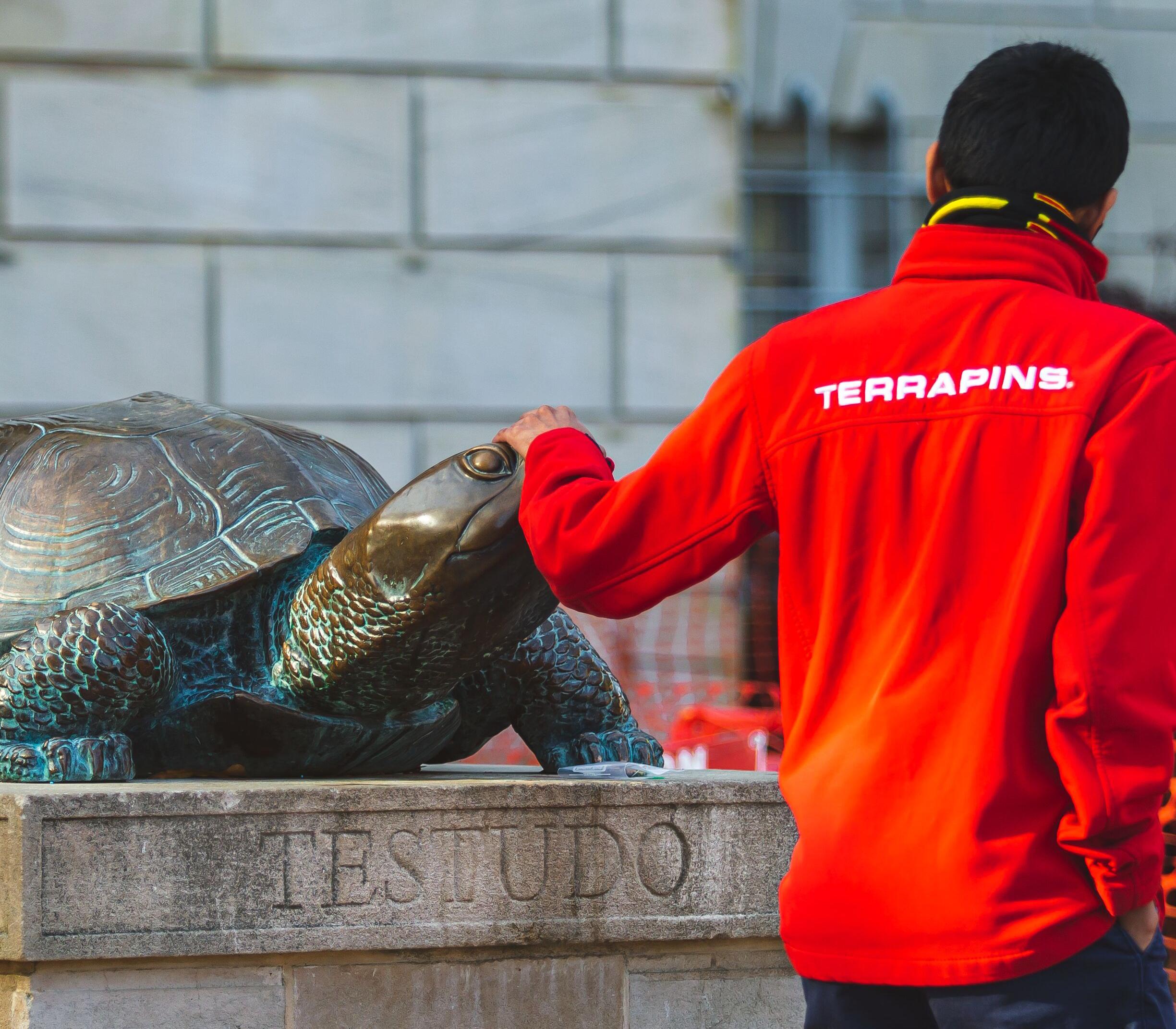 Male student wearing a red jacket rubbing Testudo’s nose in front of McKeldin Library.Student rubbing the nose of Testudo statue outside of McKeldin Library.