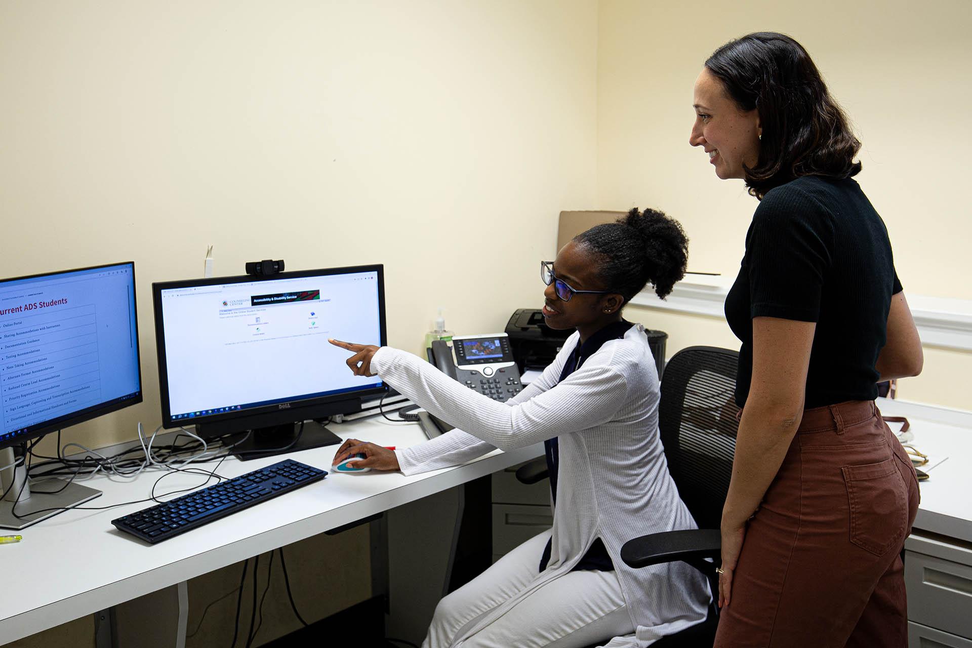 two disability specialists, one sitting and the other standing, reviewing something on a desktop